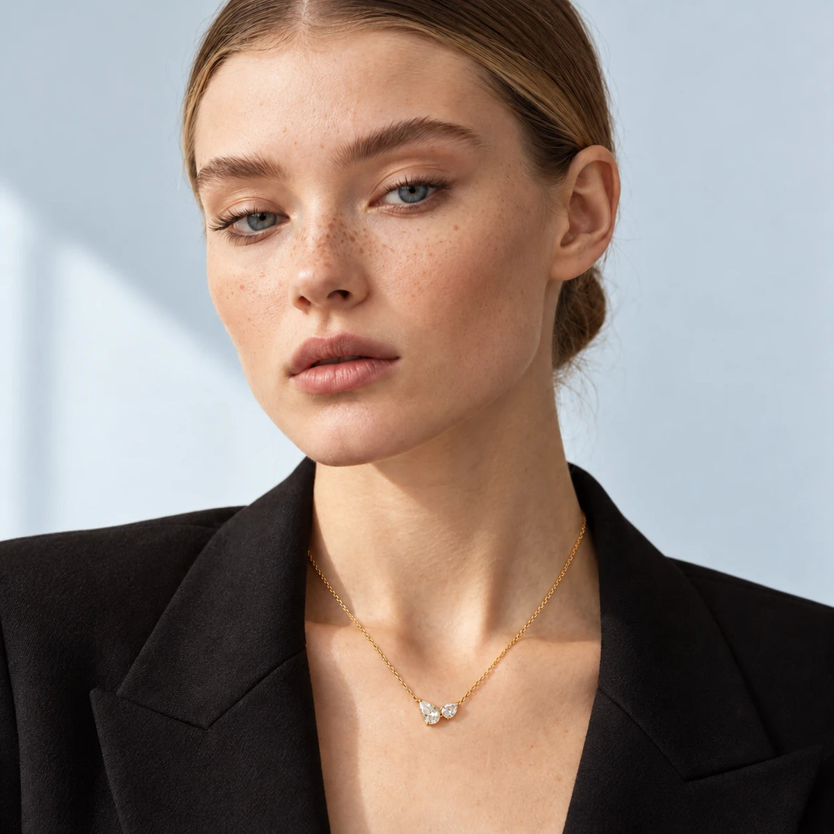 Mara wearing the Lucía double pear moissanite necklace in gold against a pale blue-grey background