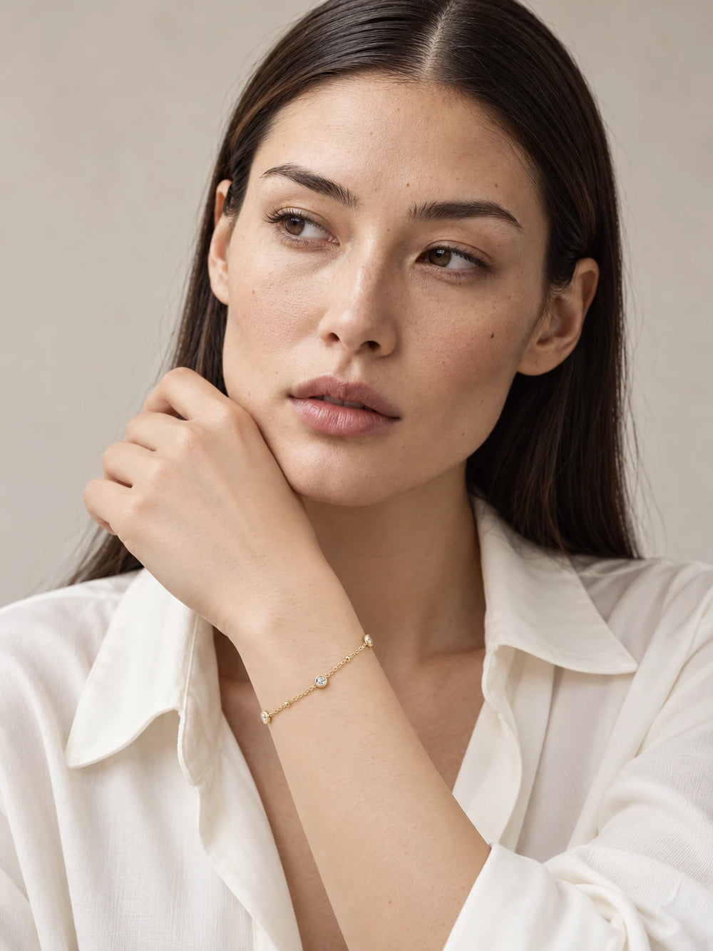 Pilla looking slightly away while wearing Nyla gold bracelet with three petite round bezel moissanites and small gold chain accents